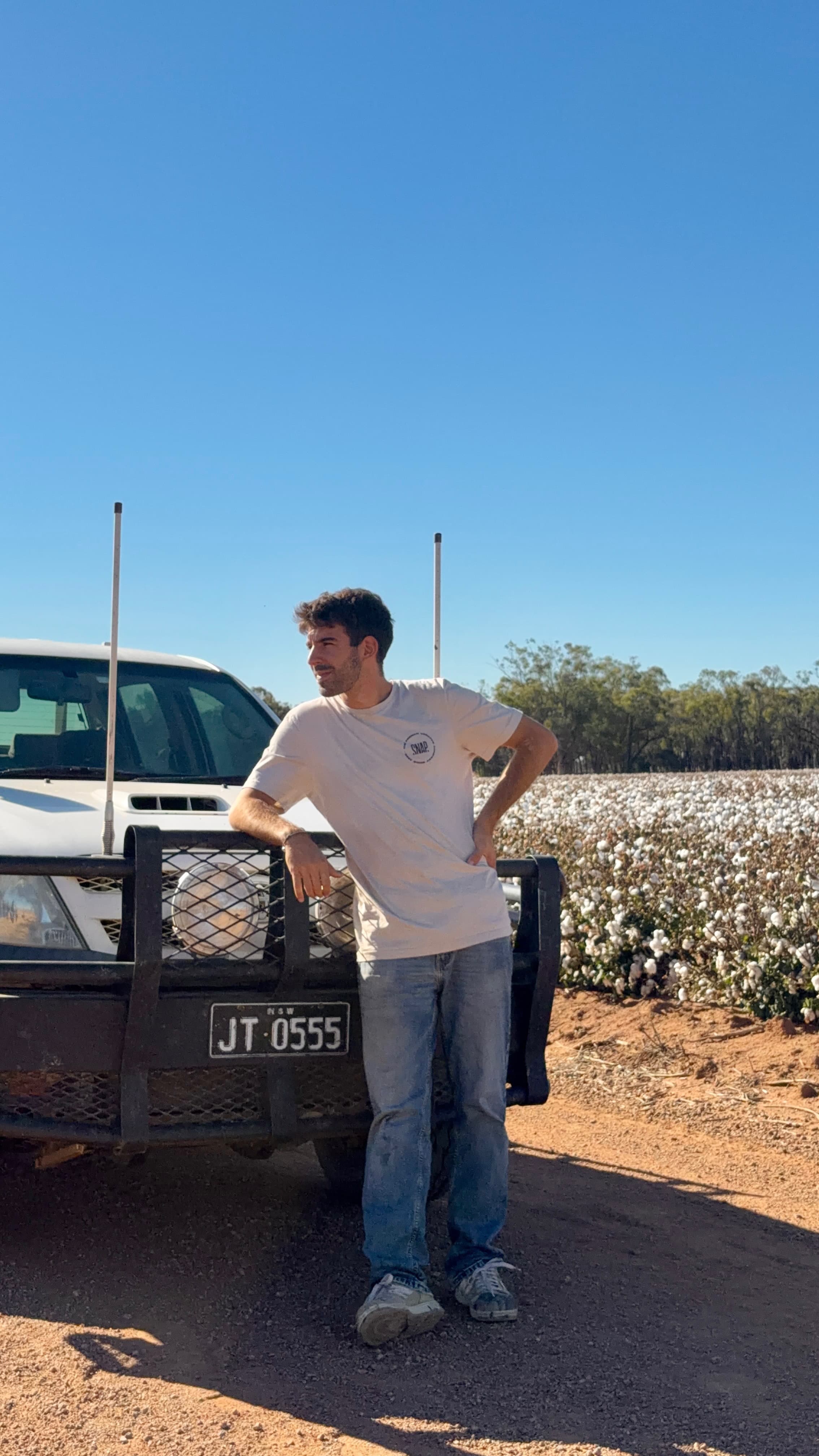 Portrait of Martin De Queiroz leaning against a pickup truck in front of a cotton field